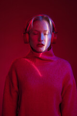 A serious woman listening to music while looking at the camera isolated on magenta background. Viva magenta, color of the year.