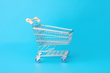 Caddie vide de supermarché à roulettes dans un fond de couleur uni bleu