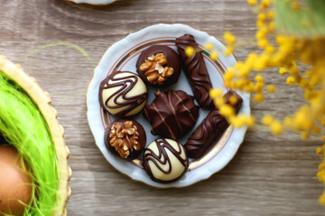 Easter eggs in the basket, bowl of cookies, chocolate pralines, Easter bunny figurine, cups of tea, glasses of juice, flowers and lit candles on the table. Top view.