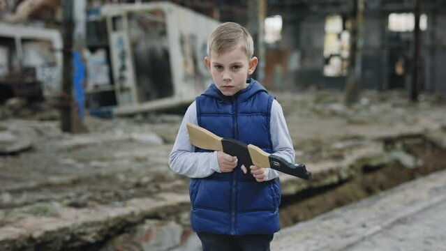 Portrait of the male child holds a toy gun against a background of devastation place. Boy games. War. Boy playing in water standing in the destroyed plant