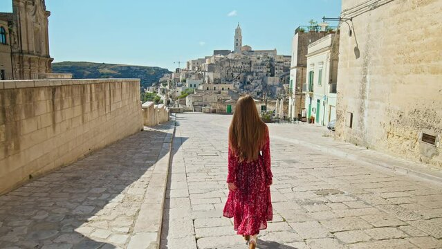 A young woman looking at the gorgeous old town, Sassi di Matera. A female tourist exploring the city on a rocky outcrop with a complex of cave dwellings carved into the mountainside in Matera, Italy.