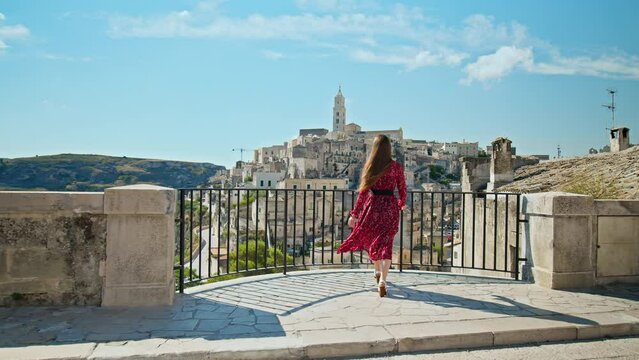 A young woman looking at the gorgeous old town, Sassi di Matera. A female tourist exploring the city on a rocky outcrop with a complex of cave dwellings carved into the mountainside in Matera, Italy.