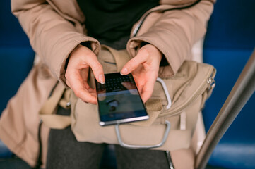 A young woman rides in a modern subway car with a phone in her hands. Close-up of hands with phone