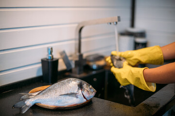 Close-up of hands and fish. A young woman cleans fish at the sink in the kitchen.
