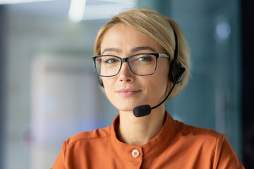 Close-up photo. Portrait of a young woman in a headset, glasses and an orange shirt looking at the...