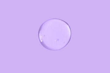 A large round drop of a transparent cosmetic gel on a purple, lilac background.