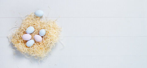 Pastel blue and pink Easter eggs in nest on white wooden background. Top view with copy space  Easter banner