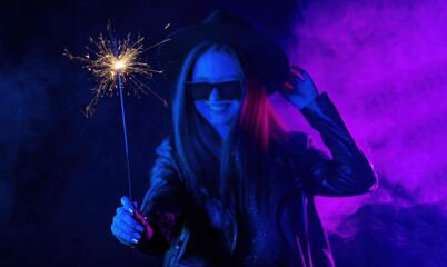 Stylish woman in eyewear dancing with bengal sparkler fire under neon light.