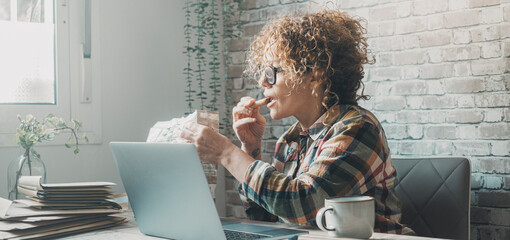 One woman at the table eating chocolate cookies in work break. Female people working with laptop...