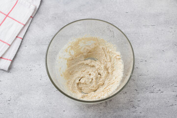 Glass bowl with dough on a gray background. Cooking greek easter orange sesame koulourakia cookies step by step instruction. Do it yourself. Step 1. Beat butter with sugar