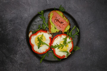 Breakfast plate with fried eggs, red pepper, salmon sandwiche and avocado on black background.