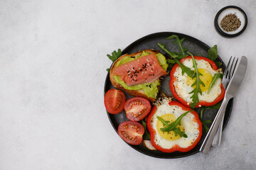 Breakfast plate with fried eggs, red pepper, salmon sandwiche and avocado on grey background.