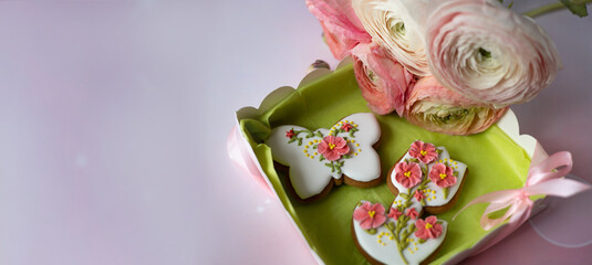 Handmade gingerbread butterfly and tulip in gift box next to bouquet of ranunculus asiaticus flowers on pink background. Beautiful gifts for Mother's day, March 8, birthday, Valentine's day. Banner