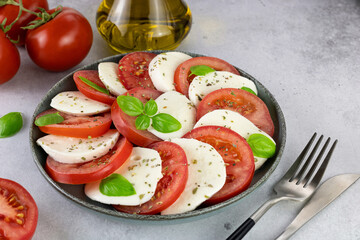 Italian caprese salad with tomatoes, mozzarella, basil, olive oil on a gray background. Italian food.