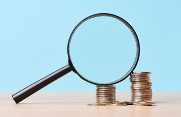 A stack of metal coins and a plastic magnifier on a blue background. The concept of increasing...