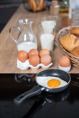 Various breads in baskets, 2 glasses and a mug with milk, oranges in a black dish and some eggs on the wooden table.