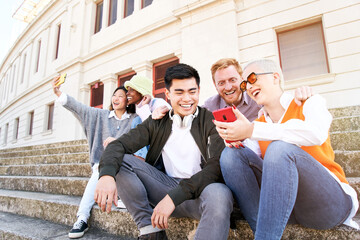 Smiling woman showing something funny on mobile phone to multi-ethnic friends. Happy group of multiracial colleagues outdoors using and holding mobile. Young people addicted to social networks.