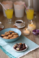 Plate of chocolate pralines, bowl of cookies, cups of tea, glasses of juice and lit candles on the table. Selective focus.