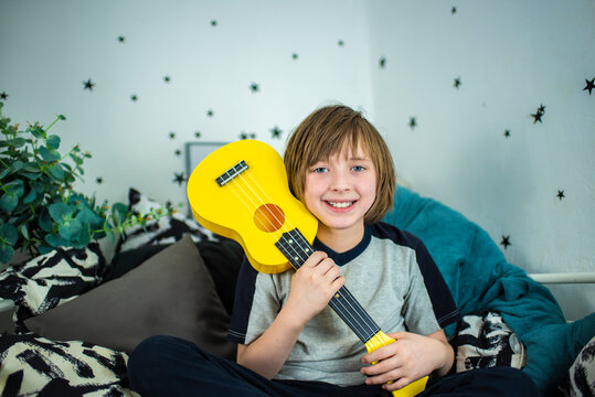 a little boy hugs a yellow ukulele, a happy child sits in his bed, on black and white bedding, plays the mini guitar and sings