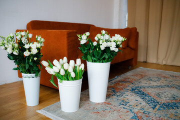Spring flowers of eustoma and tulips in vases at home. A brown sofa with an antique rug