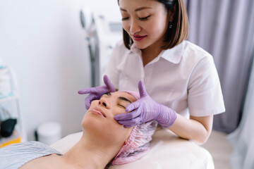 Crop positive Asian beautician doing massage to client