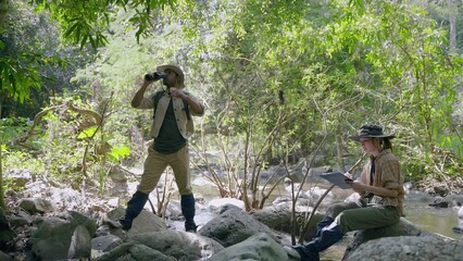 couple biologist on a forest walk collecting data is using binoculars to look into the treetops, conservation concept, green, environment.
