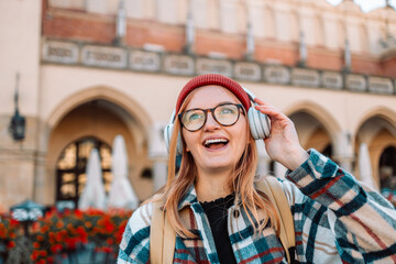 Young blonde woman smiling happy using smartphone and headphones, posing in street of European Krakow city. High quality photo