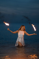 Fototapeta na wymiar Caucasian woman in a white dress juggles with fireballs in the sea. Fire and water at night. Fire show on the waterfront. High quality FullHD footage. slow motion video