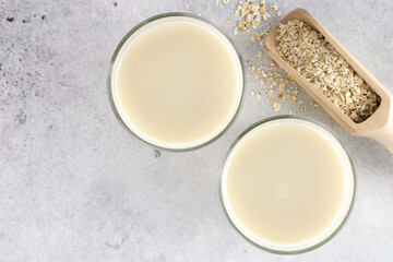 Two glasses of oat milk and oatmeal on a gray background. Top view. Copy space. The concept of alternative lactose-free dairy products.
