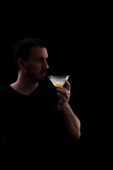young man in a black shirt with a glass of martini isolated on a black background
