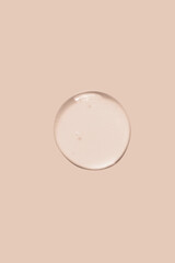 Large round drop of transparent cosmetic gel on a beige background