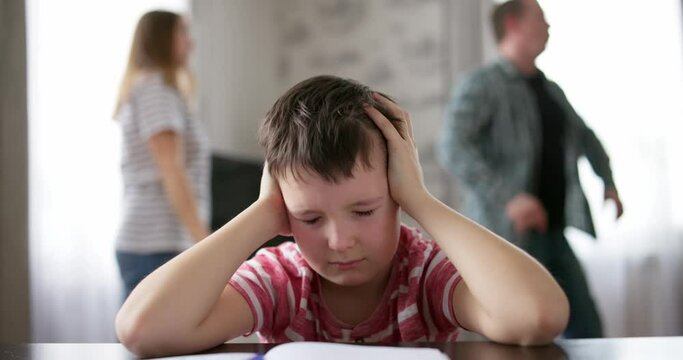 Sad child covers his ears with his hands during an argument between his parents