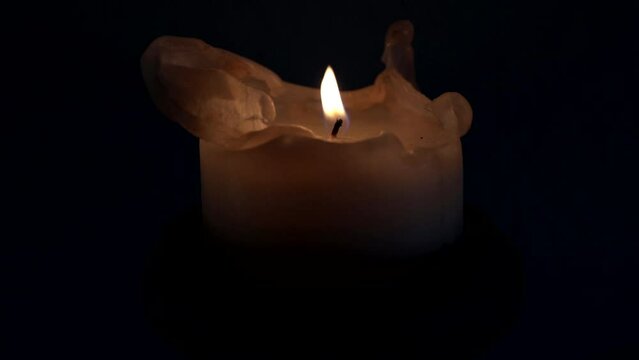 A gust of wind extinguishes the flame of the candle burning in the dark night.