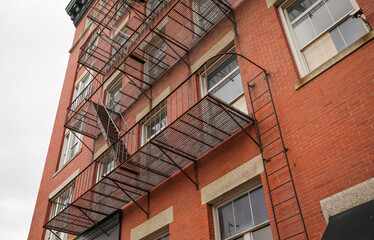 view of fire escapes on buildings and houses. A series of metal ladders and platforms are visible on the exterior walls of the structures. Captures the urban aesthetic of the fire escape.