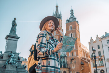 Real view of traveller woman walking on old Market Square in Krakow holding tourist map. Travel and active lifestyle concept. High quality photo