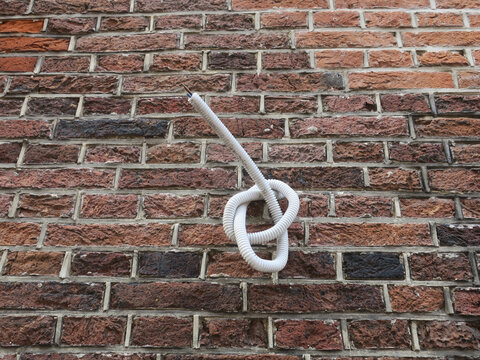 knot of electricity cable peeping out of a hole in a brick wall