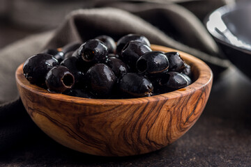 Pitted black olives in wooden bowl on kitchen table.