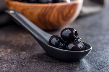 Pitted black olives in ceramic spoon.