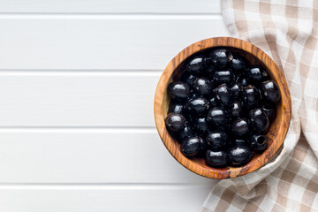 Pitted black olives in wooden bowl on kitchen table. Top view.