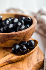 Pitted black olives in wooden spoon.