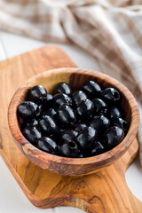 Pitted black olives in wooden bowl on kitchen table.