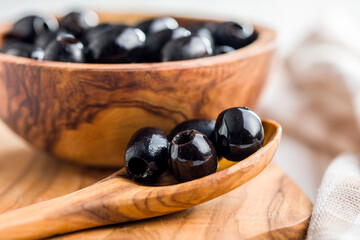 Pitted black olives in wooden spoon.