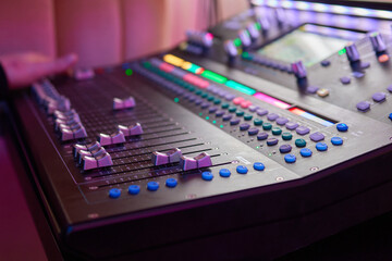 An expert adjusting audio mixing console with white blank screen laptop on control desk.
