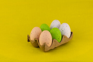 Easter eggs in a cardboard box on a yellow background. Painted in different colors, speckled eggs lie in a cardboard tray on an isolated yellow background. Easter concept.