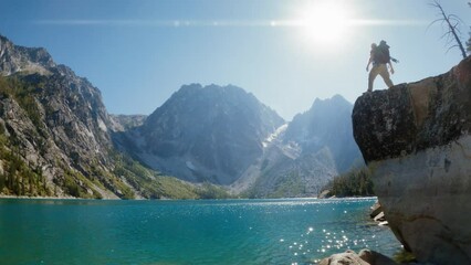 Hiker Walks to Rock Edge for View of Turquoise Alpine Lake