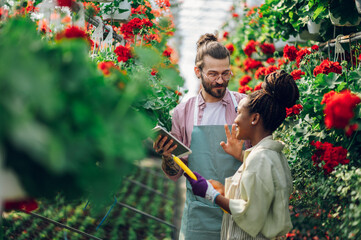 Multiracial couple of gardeners working in a greenhouse and using tablet