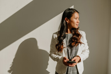 Asian businesswoman using smartphone while standing over a white wall in an office