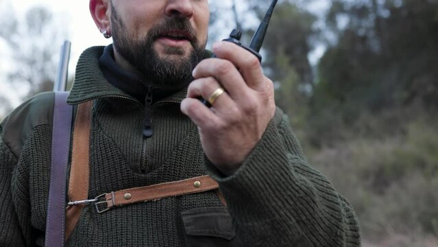 Close up view of a hunter man talking to someone on a walkie talkie outdoors.