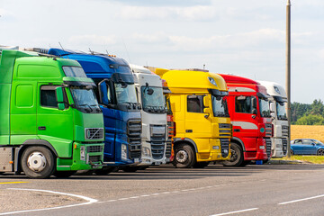 Trucks with containers in the parking lot along the highway against the background of clouds. The concept of logistics, transport and cargo transportation. The resting place of trucks in the parking
