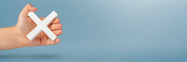White multiplication symbol or cross in hand. The concept of prohibition or removal. Mathematical white symbol multiply in hand on a blue background